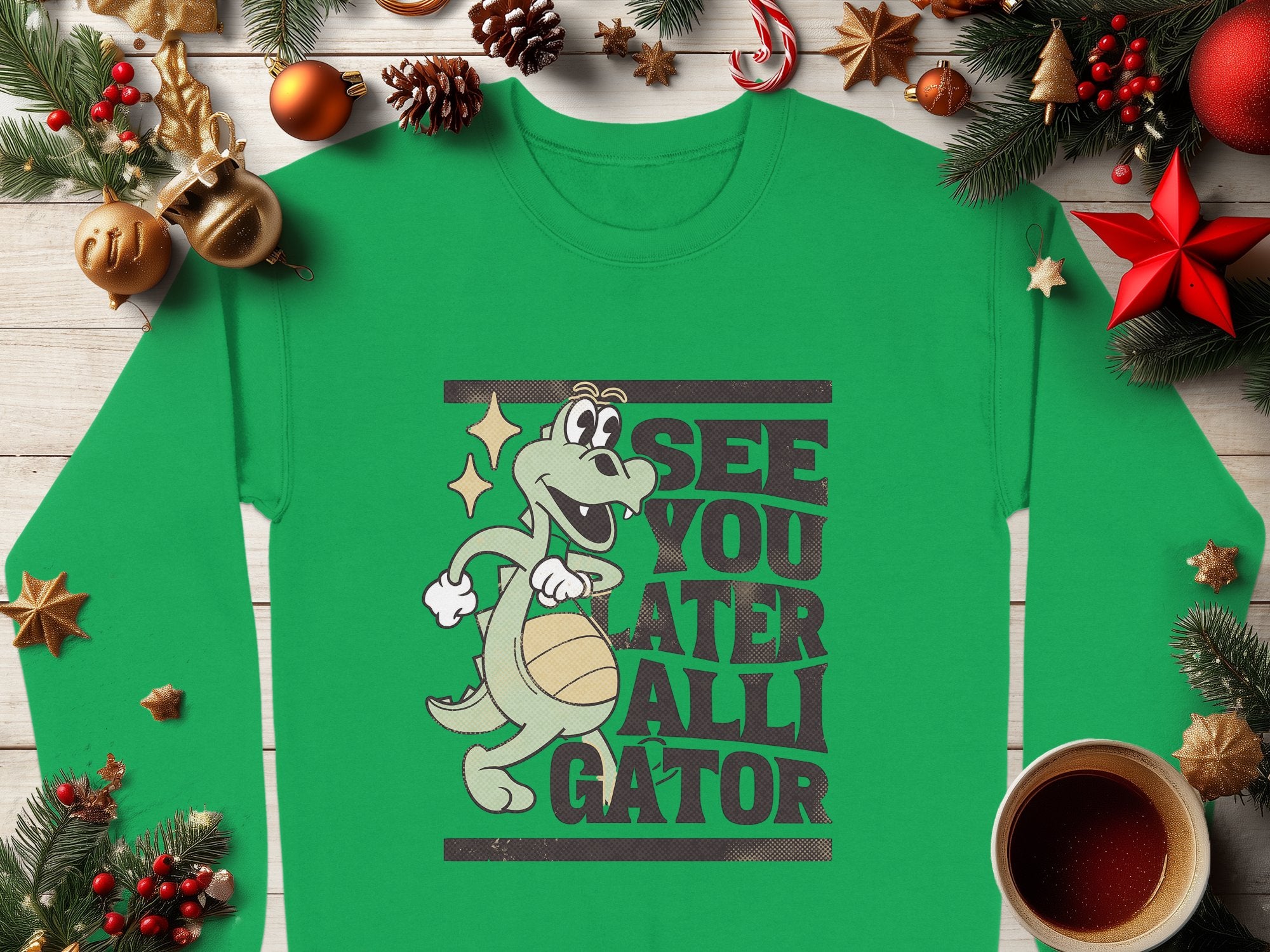 Garment Graphics offers a festive green unisex sweatshirt featuring a cartoon alligator with a basketball and playful See You Later Alligator text, surrounded by pine branches, ornaments, and a warm coffee cup for seasonal cheer.