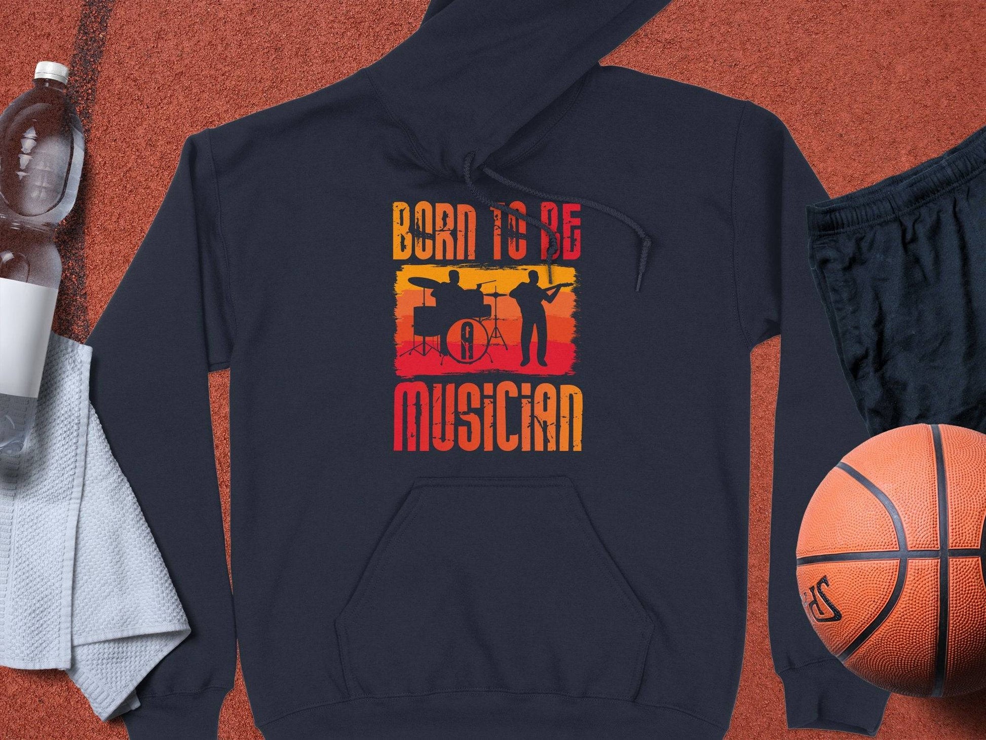 The black hoodie from Garment Graphics is perfect for music lovers, featuring a graphic of musicians and the text Born to Be Musician. Ideal for unisex fashion fans, its displayed with a basketball, black shorts, a towel, water bottle, and white cap.