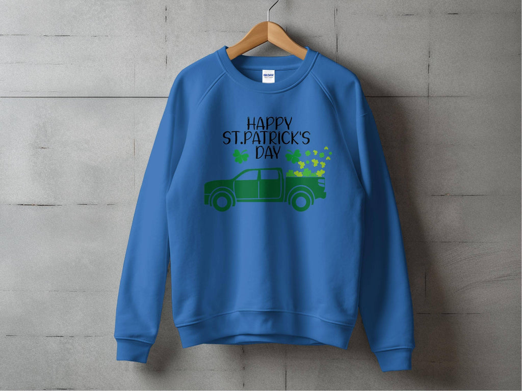 A blue festive sweatshirt by Garment Graphics hangs against a concrete wall, showcasing a green truck with shamrocks. Happy St. Patricks Day is elegantly displayed in black text above the truck, capturing the holiday spirit.