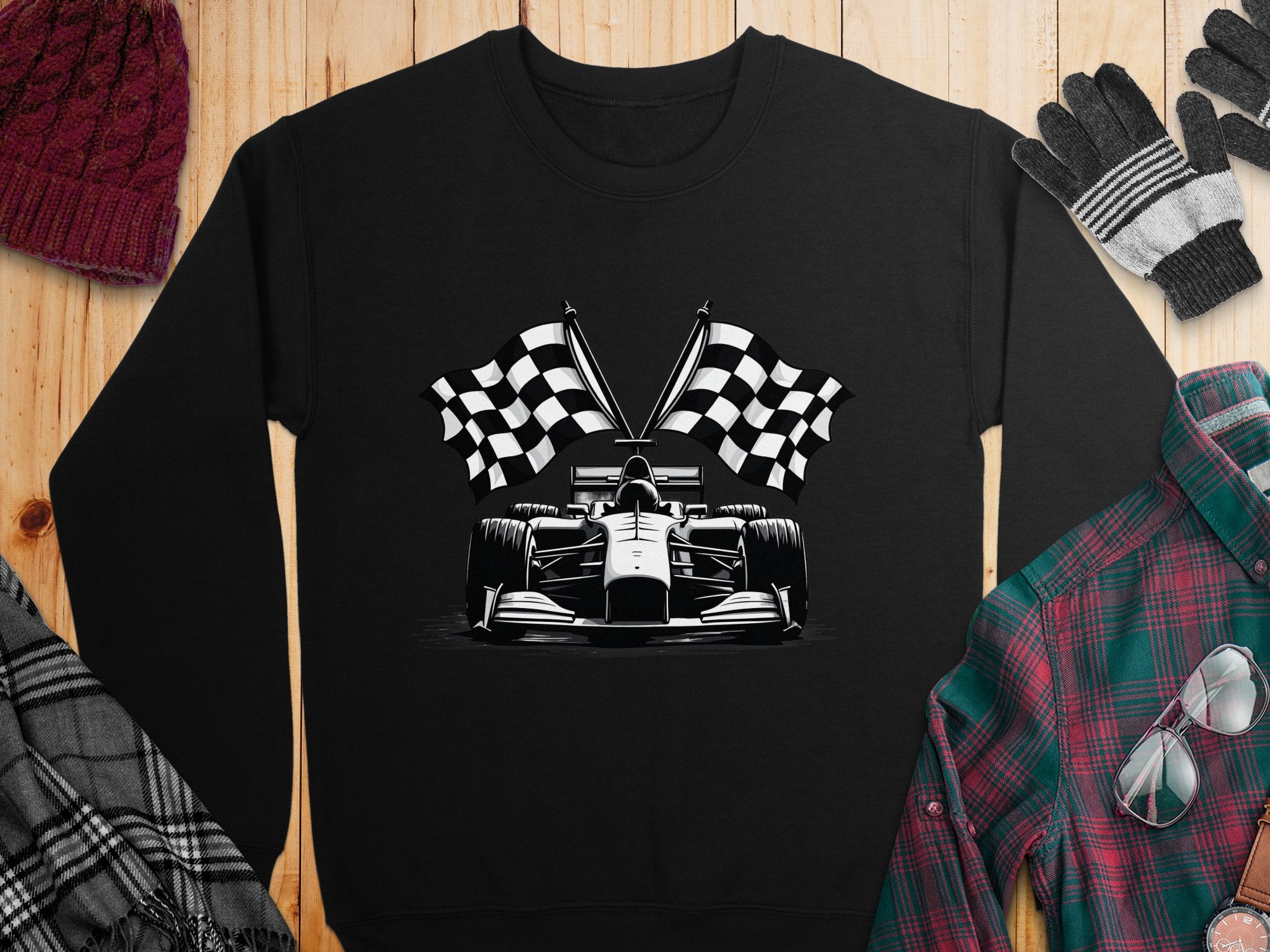 Garment Graphics presents a black racing car sweatshirt featuring a large Formula 1 car graphic with two checkered flags. Laid on wood, it’s paired with a knitted hat, gloves, and plaid shirt for a style statement.
