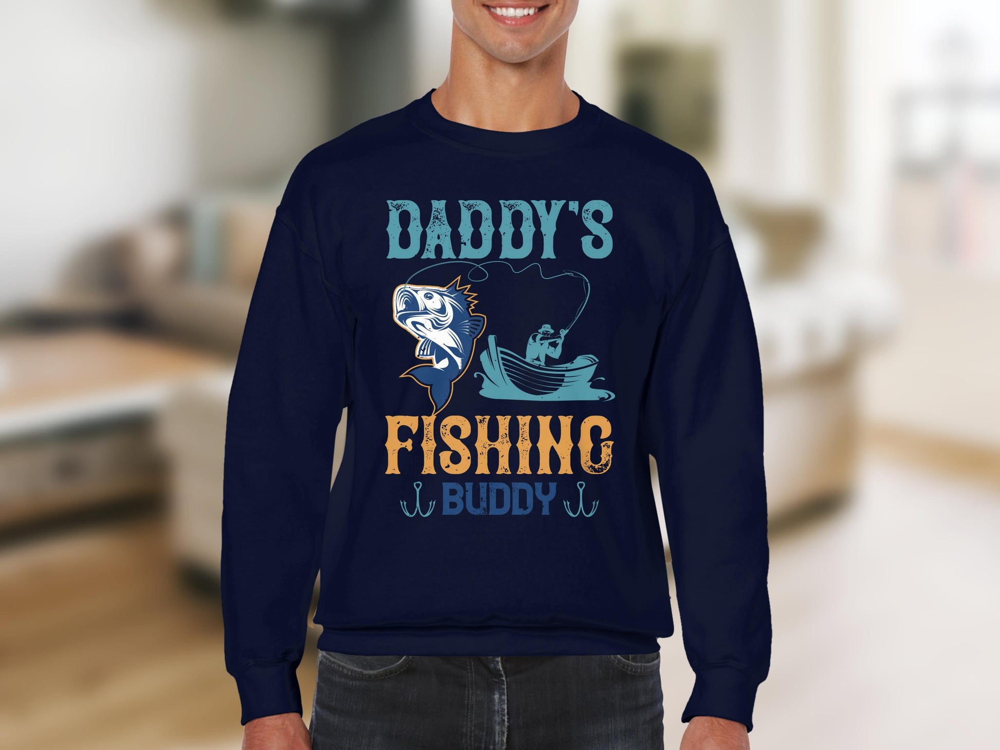 Someone wears a Garment Graphics navy blue fishing sweatshirt with Daddys Fishing Buddy, featuring a fish and boat design. The softly blurred interior background sets the scene for fishing enthusiasts cherishing their bond on the water.