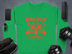 The unisex green football sweatshirt by Garment Graphics features red text: Born to Play, One Goal - One Dream, Young Squad Football, Kick. Score. Celebrate! It is surrounded by a smartphone, smartwatch, portable speaker, dumbbells, and black shoes on a gray background—ideal for young squads!.