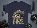 A classic fit navy T-shirt from Garment Graphics, showcasing a gem-encrusted eye design with GAZE beneath, features on a gray surface surrounded by a smartphone, wireless speaker, smartwatch, sneakers, earbuds, and dumbbells.
