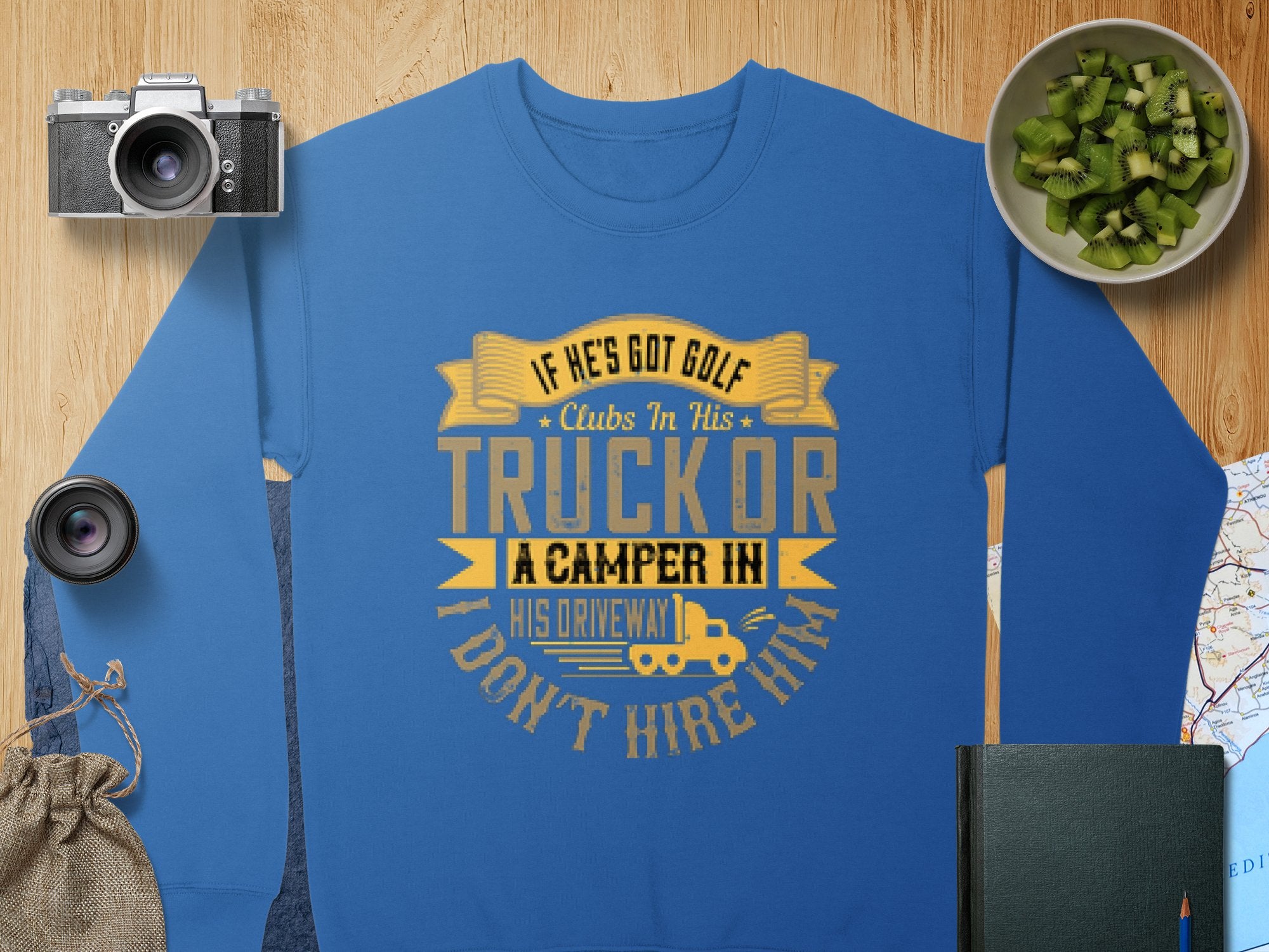 Garment Graphics offers a blue sweatshirt with a humorous gold graphic: If he’s got golf clubs in his truck or a camper in his driveway, I don’t hire him, surrounded by a camera, lens, cucumber slices, drawstring pouch, map, and notebook on wood.