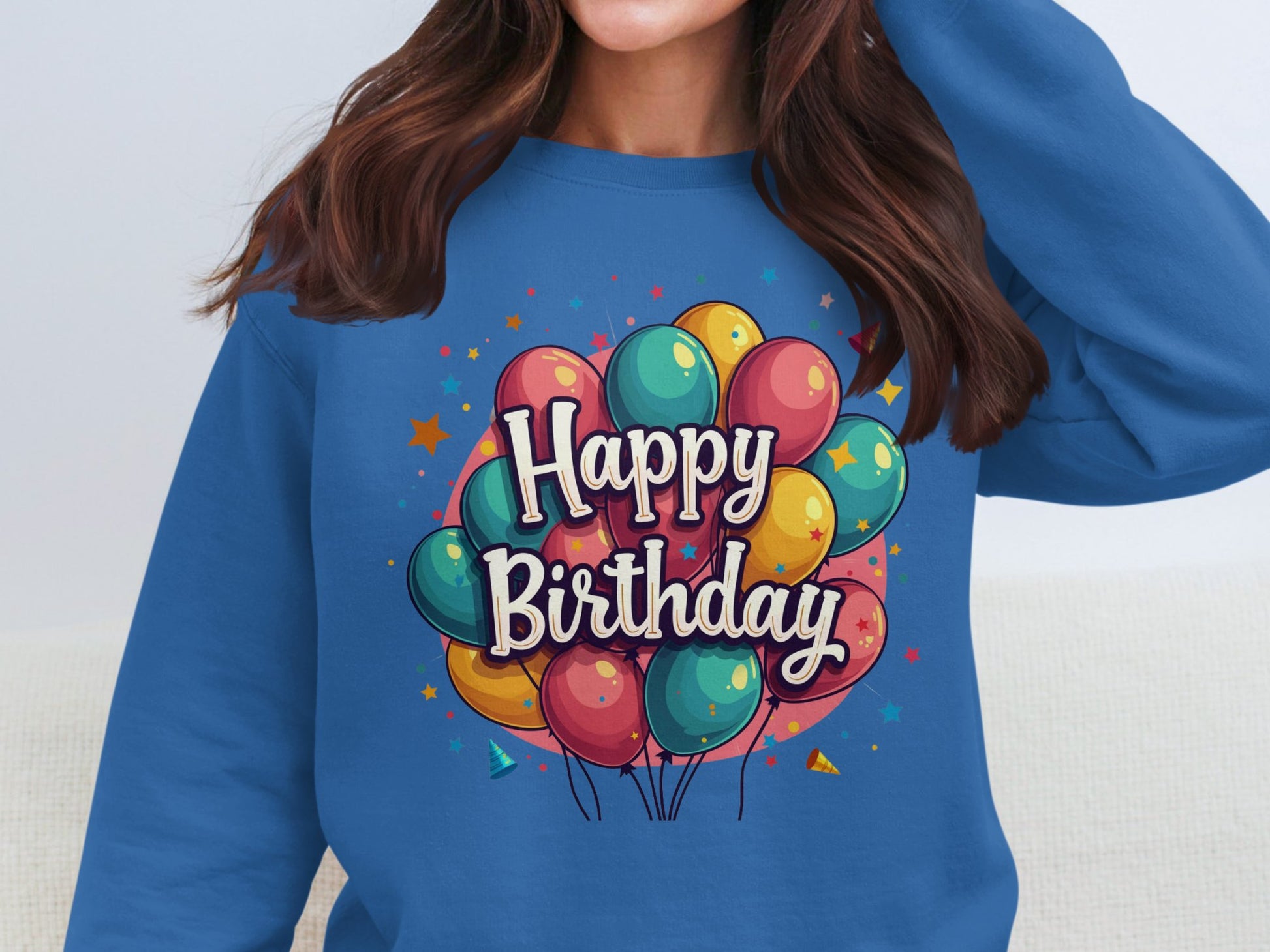 A person with long brown hair joyfully celebrates in a blue Garment Graphics Happy Birthday sweatshirt. It features a vibrant balloon design and unisex sizing, making it perfect for any celebration.