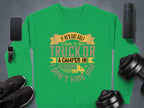Garment Graphics presents a green sweatshirt featuring a humorous graphic: If hes got golf clubs in his truck or a camper in his driveway, I dont hire him, surrounded by a smartphone, speakers, sneakers, and dumbbells on a gray surface.