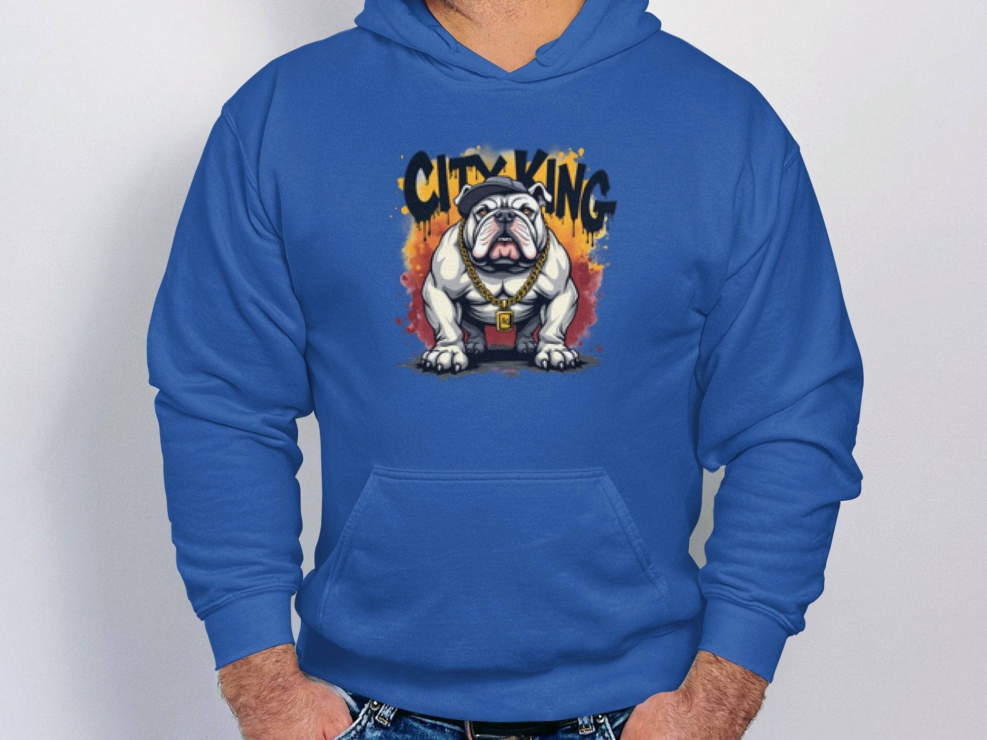 A person in a blue hoodie from Garment Graphics Graphic Bulldog Design collection sports a bulldog with sunglasses and a gold chain. The designs graffiti-style, featuring vibrant orange and yellow accents, enhances any casual wardrobe with its classic fit and City King branding.