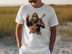 A person is wearing a Garment Graphics white T-shirt showcasing a cartoon gorilla with sunglasses, holding an electric guitar, and making a peace sign against a blurred grassy landscape—ideal for music enthusiasts.
