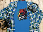A blue t-shirt with an eagle design and Garment Graphics sits on a plaid shirt on a wooden surface. A camera, headphones, and lidded coffee cup complete the scene, capturing this stylish classic fit ensemble.