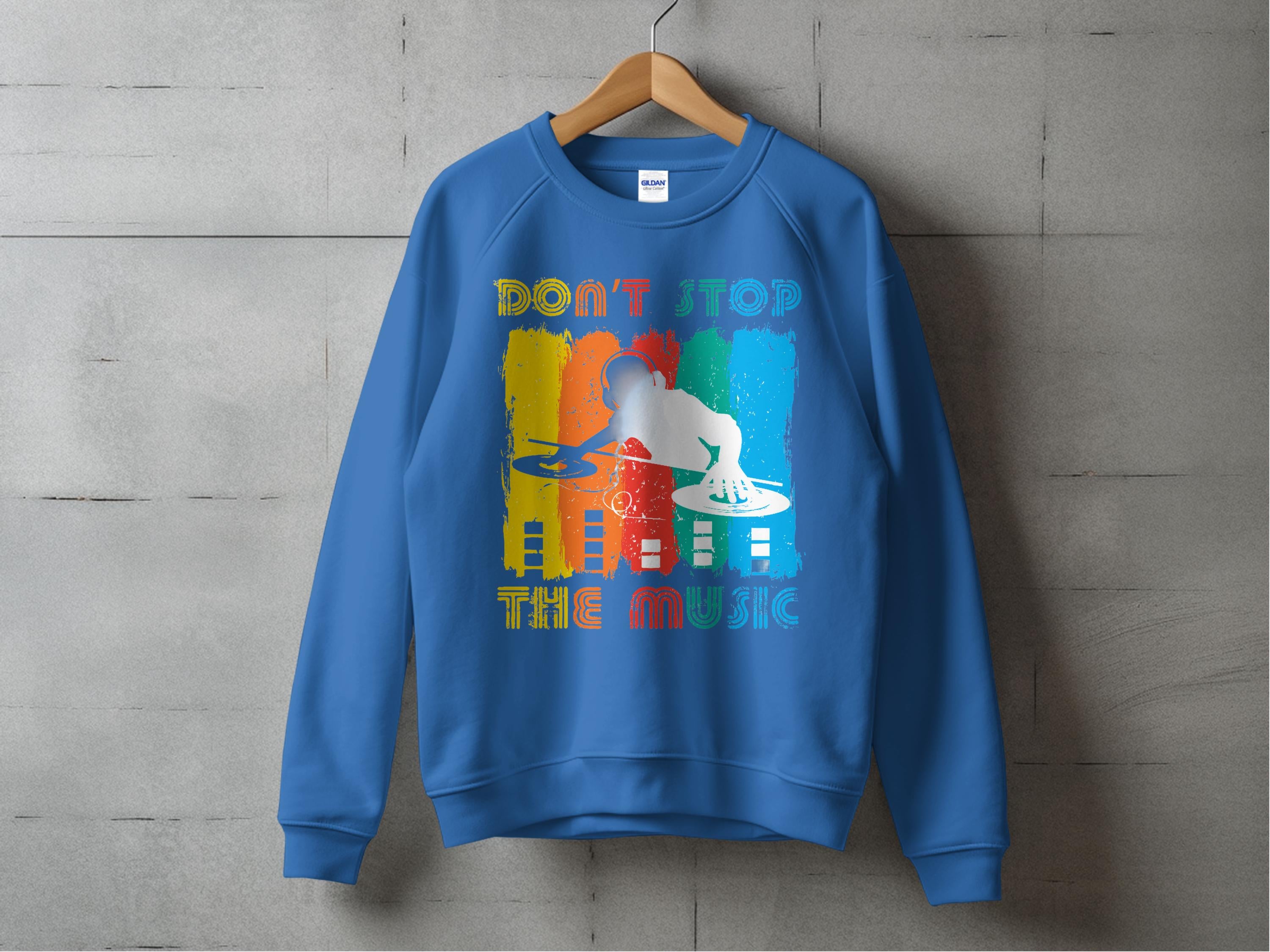 The Garment Graphics blue sweatshirt features a vibrant DJ design with a silhouette on the turntable and Dont Stop the Music above. Its an ideal choice for music enthusiasts, elegantly displayed on a wooden hanger against a concrete background.