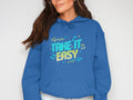 A woman confidently rocks her vibrant casual style in a blue Garment Graphics hoodie, featuring the phrase Take It Easy in colorful letters and small decorative elements. Her long brown hair adds to her effortlessly chic look against a plain background.