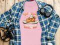 A Garment Graphics plaid shirt, a pink T-shirt with Hot & Spice, You Wanna a Piece of Me? graphic, headphones, and a camera lie on wood. Perfectly sized for women and ideal for casual outings.
