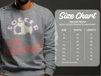 A person wears a gray Soccer Dad sweatshirt from Garment Graphics, featuring a soccer ball design. Next to them is a size chart for these trendy unisex sweatshirts, available in sizes S to 5XL with width and length measurements in inches.