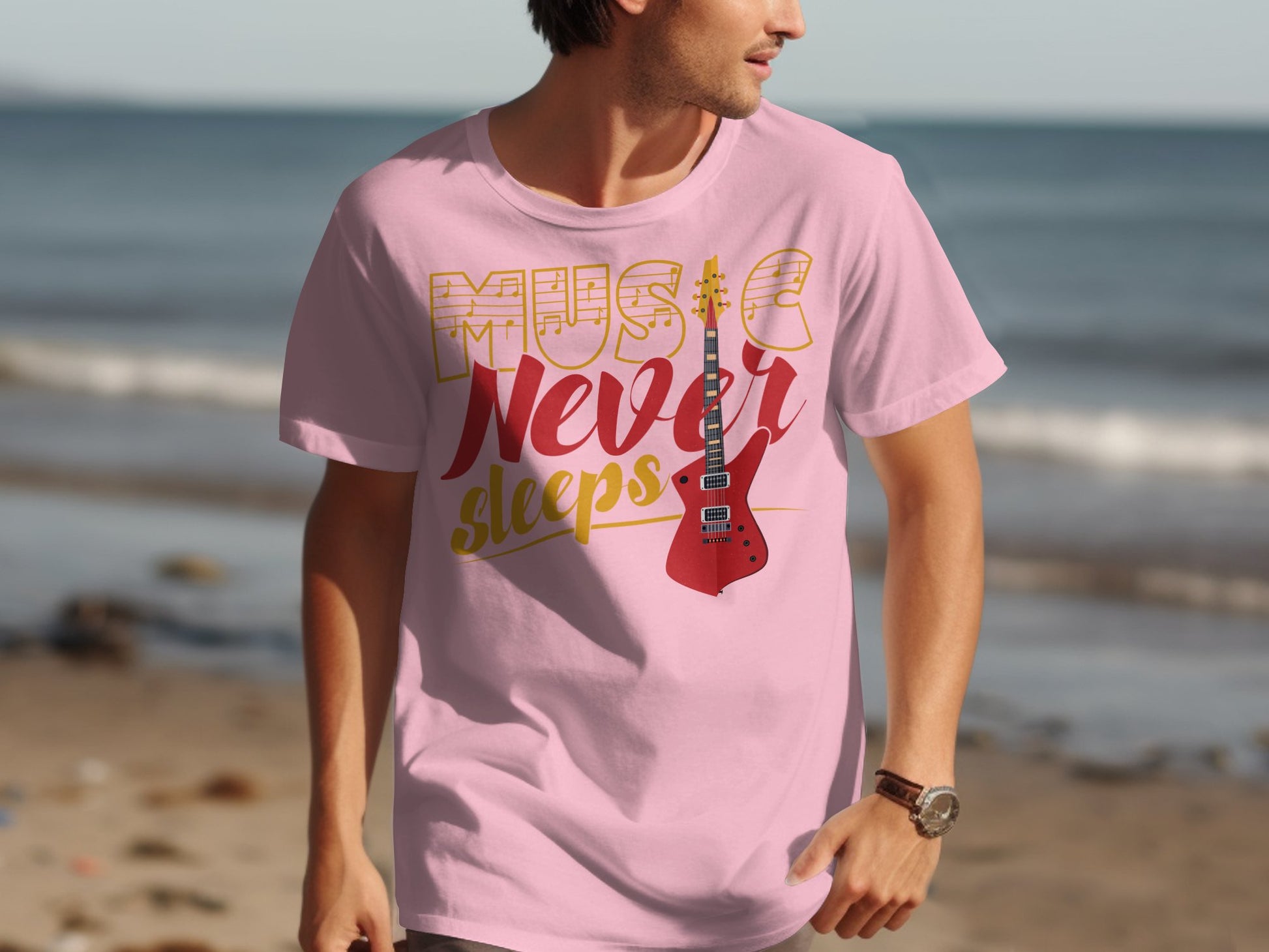 A man walks on the beach in a Garment Graphics pink 100% cotton tee reading Music Never Sleeps. The shirt features a bold red guitar, creating a striking scene against the sea and sand.