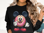 The individual in a black sweatshirt from Garment Graphics showcases a playful donut character with mouse ears, a pink sprinkle face, and red shoes. Highlighting whimsical charm by clasping their wavy hair, this unisex piece ensures everyone can enjoy the fun design.