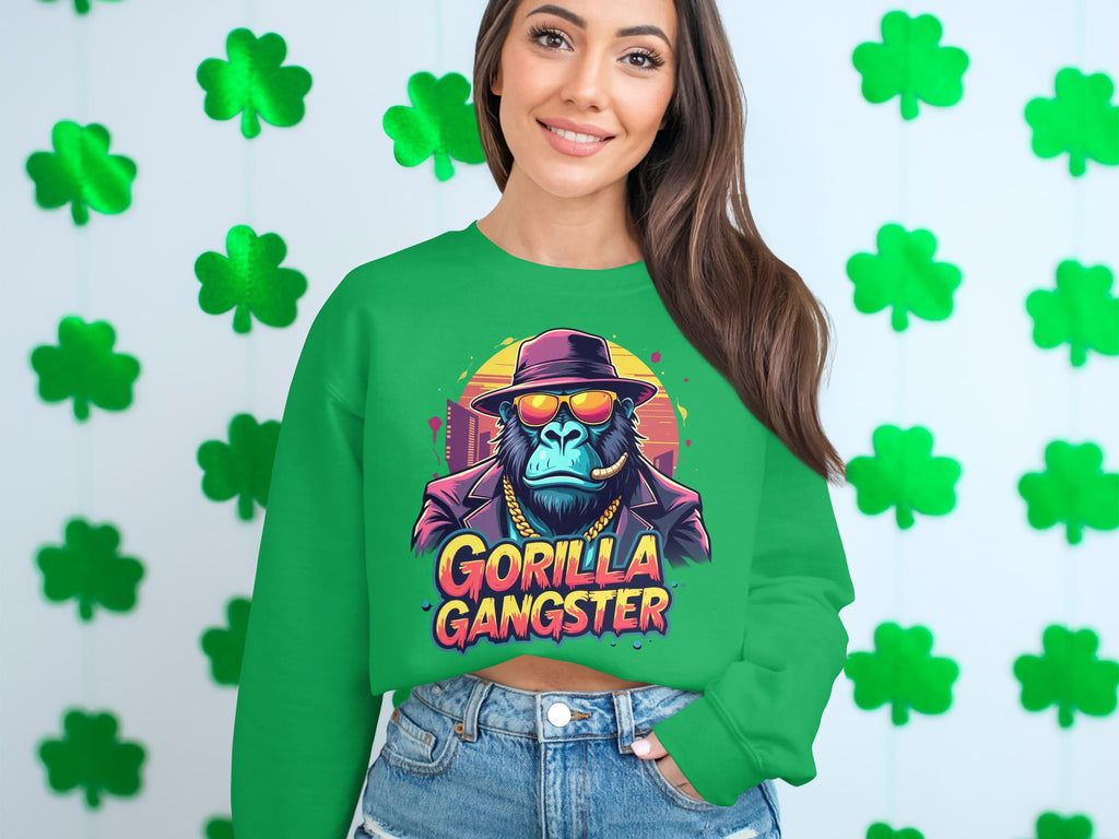A woman sports an urban-chic Garment Graphics green sweatshirt, showcasing a gorilla gangster with hat and sunglasses. The striking Gorilla Gangster text stands out as she poses before vibrant green shamrocks.