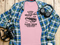 A pink Classic Fit T-shirt from Garment Graphics with a vintage car design and text Classic London City Vintage Car Club and Classic Garage is displayed on a blue plaid shirt, alongside a camera, headphones, and rustic wooden planks in the background.