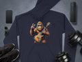 The Garment Graphics navy electric guitar hoodie showcases a cartoon gorilla rocking out and flashing a peace sign. Its perfect for music lovers and pairs well with a smartphone, fitness tracker, speakers, sneakers, and dumbbells on a gray surface.