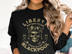 A person with wavy blonde hair is rocking a biker look in a black Garment Graphics sweatshirt featuring a skull with goggles and the text Liberty Motorcycles Specialist Blackpool 2023, while holding a strand of hair.