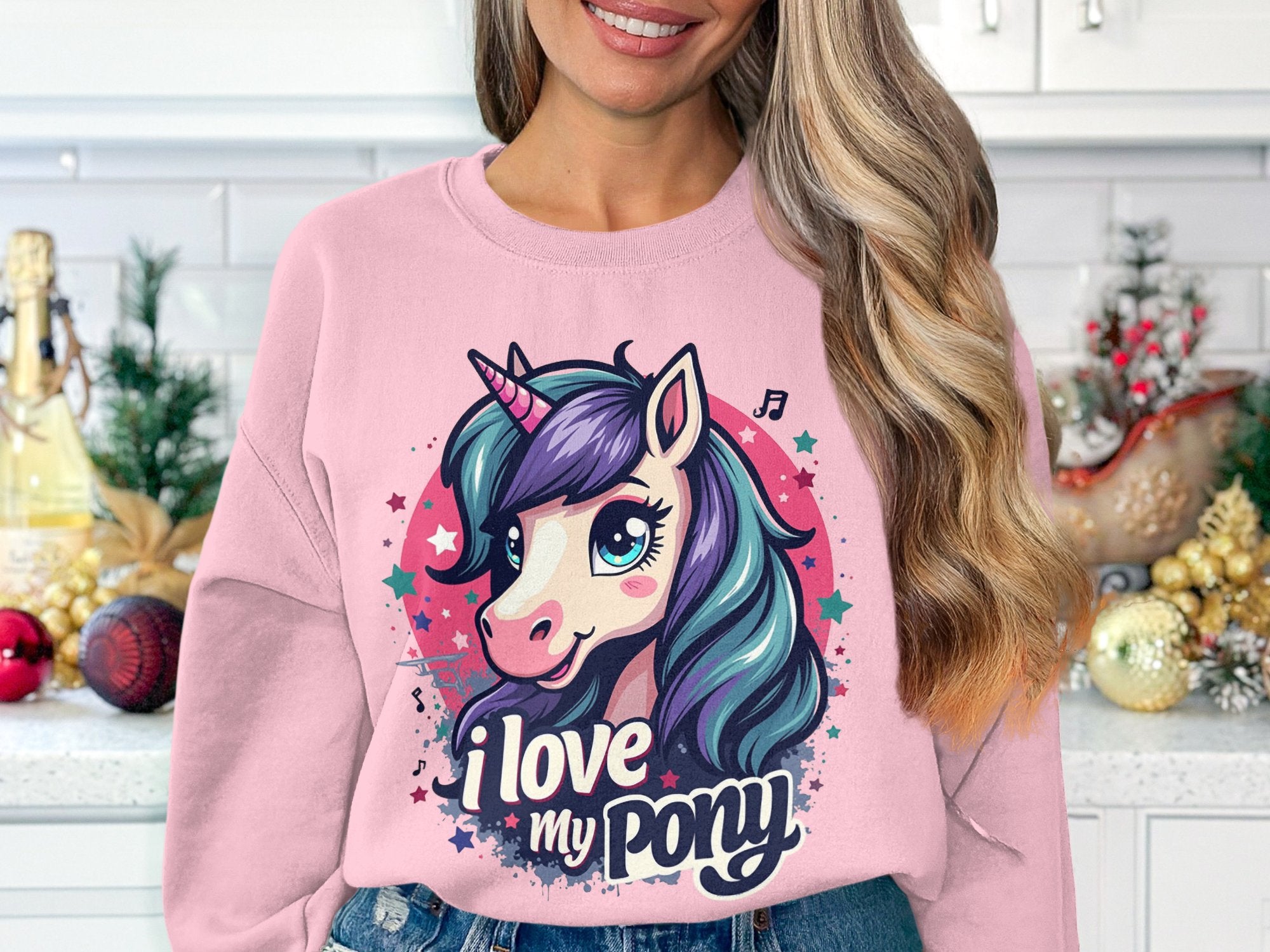 In a kitchen decorated for the holidays, someone with long, wavy hair wears a pink Garment Graphics sweatshirt featuring a colorful ponyunicorn design. Emblazoned with I love my pony, it adds charm to the festive scene.