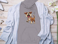 The Garment Graphics gray cartoon puppy hoodie for dog lovers is displayed on a wooden surface, surrounded by a light blue cardigan, white pointed-toe shoes, a necklace, rings, and white flowers—a truly fun addition to any wardrobe.