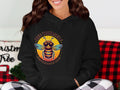 A person is wearing a Garment Graphics Bee Yourself Hoodie in black, with a colorful bee graphic. The text reads Bee Yourself above and Everyone Else is Taken below. Theyre seated on a cushioned red and black checkered surface, making the hoodie pop.