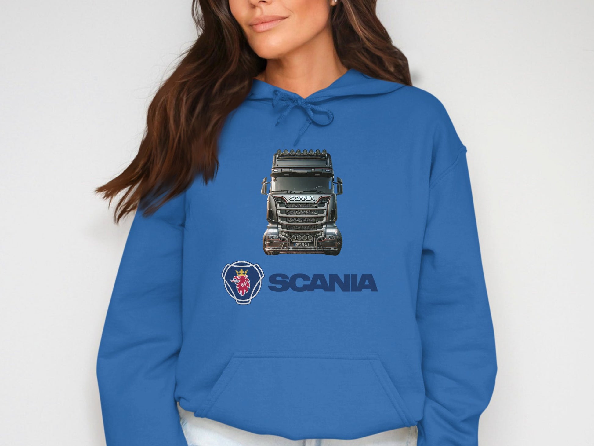 A person wears a blue Garment Graphics Scania Truck Hoodie featuring a striking graphic and logo design. The hoodie has a drawstring hood, complementing the individuals long brown hair, ideal for truck enthusiasts against a plain white background.