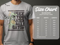 A person wears a gray t-shirt from Garment Graphics with a cartoon alligator and the slogan See You Later Alligator. The Gildan 5000 heavy cotton size chart beside them details sizes S to 5XL, ideal for casual wear seekers.