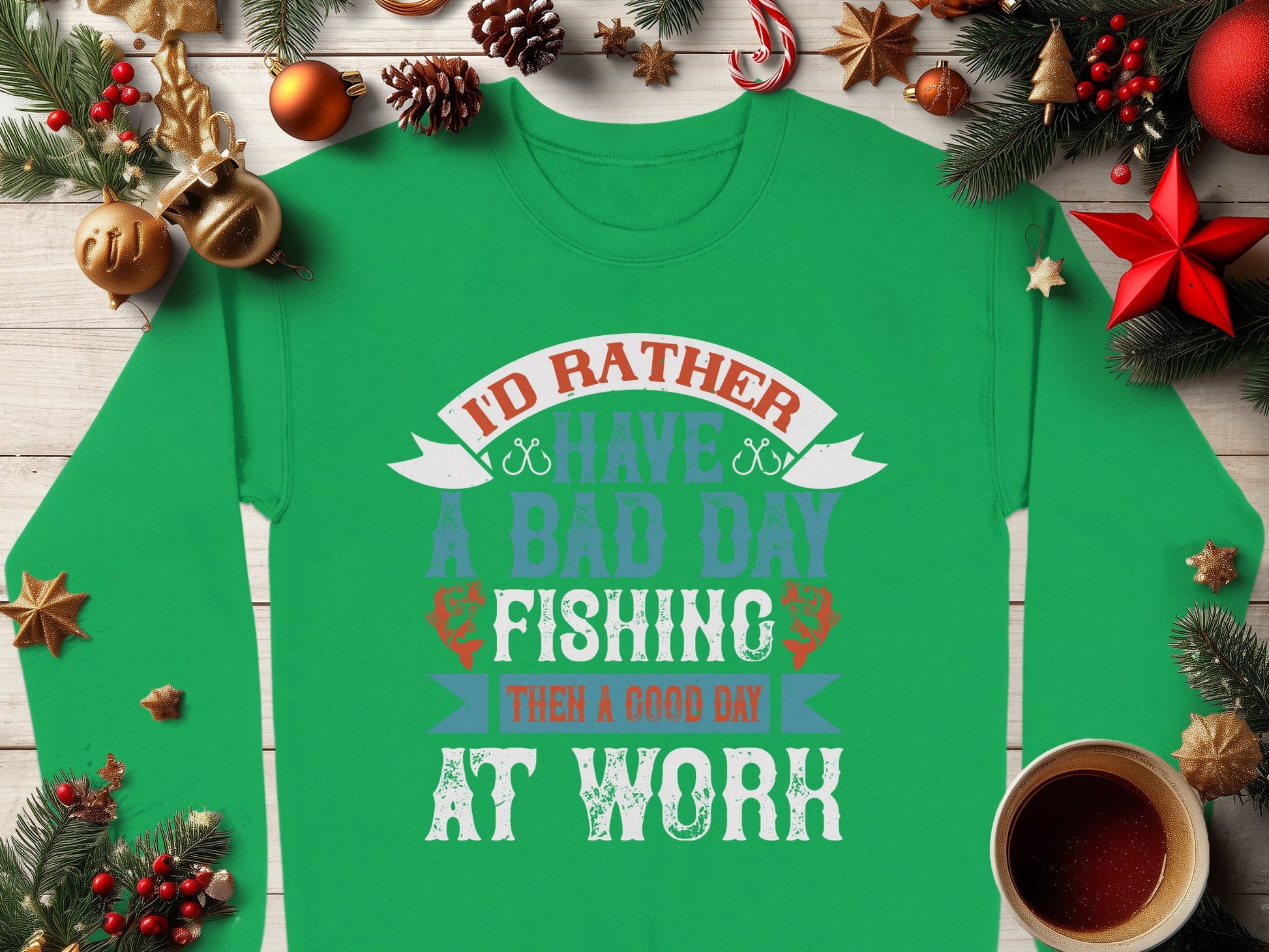 A Garment Graphics green fishing sweatshirt is displayed on wood with pine branches and ornaments. Featuring the text Id rather have a bad day fishing than a good day at work, this unisex treasure is perfect for fishing enthusiasts, with a cozy coffee cup nearby enhancing its relaxed vibe.