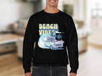 A person wears a retro roadtrip-themed black sweatshirt by Garment Graphics, featuring a pink classic car, ocean wave, palm tree, and BEACH VIBES text. The unisex-sized graphic sweatshirt is showcased with a softly blurred background.