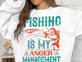 A person wears a Garment Graphics white sweatshirt adorned with Fishing is my anger management in colorful graphic text, perfect for fishing enthusiasts, featuring a fish and lure design.