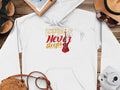 A classic fit white hoodie by Garment Graphics, featuring Music Never Sleeps with a guitar design. Ideal for travel, its styled on wood surrounded by a straw hat, sunglasses, notebook, sandals, map, camera, and a woven bag.