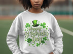 A person in Garment Graphics white sweatshirt, showcasing a St. Patricks Day design with a green hat, shamrocks, and Happy St Patricks Day text, radiates festive cheer against a blurred outdoor backdrop.