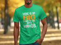 Amidst blurred autumn foliage, a person wears a bright green Garment Graphics fishing-themed tee, featuring the humorously bold text Mine is so big I have to use both hands. Its an ideal choice for fishing enthusiasts who appreciate a good laugh with their outdoor attire.