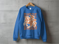 The Garment Graphics blue sweatshirt, perfect for rodeo enthusiasts, is displayed on a gray wall. It features a cowboy riding a horse illustration and the bold Howdy Rodeo text in vibrant orange, capturing the cowboy spirit.