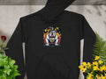 The Garment Graphics black hoodie, featuring a bold Graphic Bulldog Design called City King, is perfect for your casual wardrobe. Laid flat on concrete with green plants and yellow flowers, its classic fit offers both comfort and style.