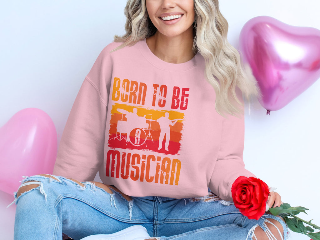 A long-haired person in a Garment Graphics unisex Born to Be Musician pink sweatshirt with a drummer graphic holds a red rose. They wear ripped jeans and are accompanied by two pink heart-shaped balloons, making it an ideal scene for music enthusiasts.