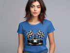 A woman with shoulder-length brown hair wears a blue Garment Graphics T-shirt depicting a race car and two checkered flags, ideal for motorsport fans. She stands against a plain gray background.