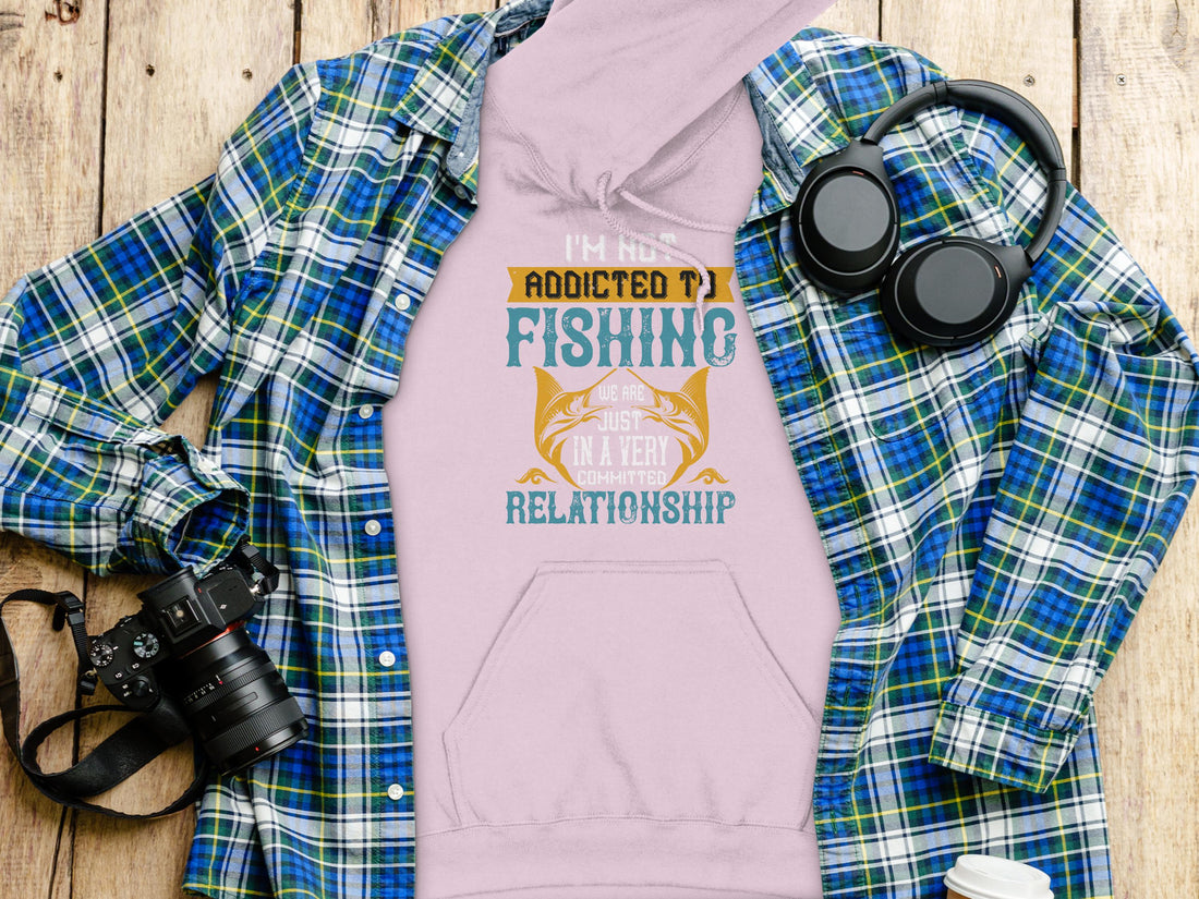 A person wears a Garment Graphics black fishing hoodie, featuring the humorous design, Im not addicted to fishing. We are just in a very committed relationship. This classic fit piece seamlessly combines comfort and style for dedicated anglers.