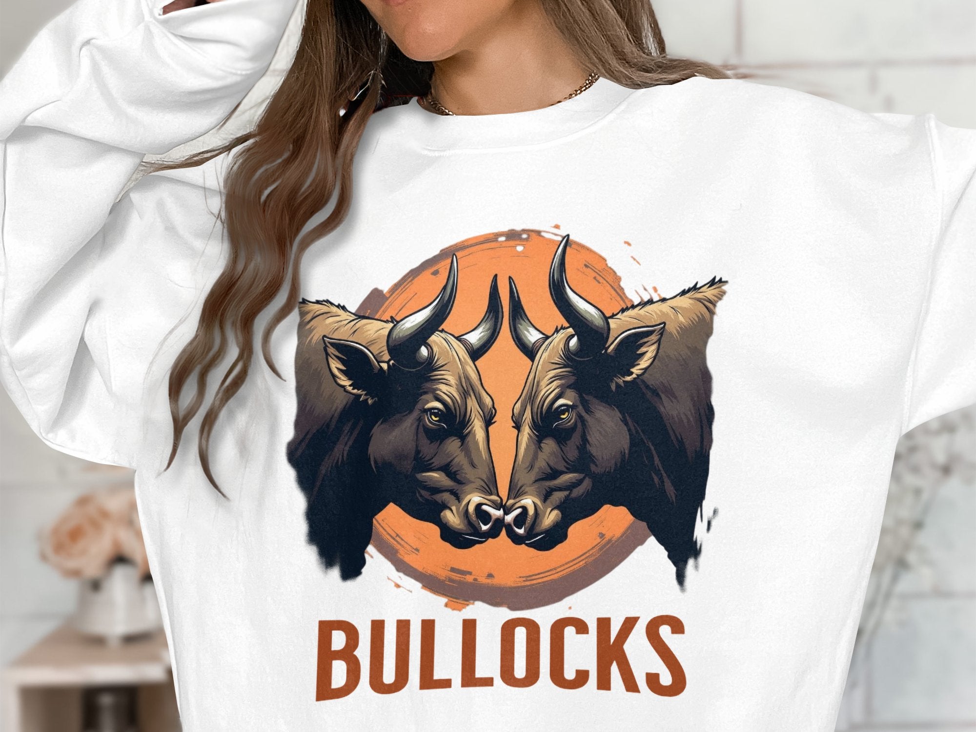 Someone is wearing a standout Garment Graphics sweatshirt featuring an illustration of two bulls facing each other against an orange circle. Below the striking bullocks graphic, BULLOCKS is boldly printed in capital letters.