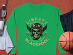 Garment Graphics presents a green sweatshirt with a unique design featuring a skull in a helmet, goggles, wings, and crossed pistons. The text reads Liberty Motorcycles Specialist Blackpool 2023. Also pictured: white towel, water bottle, black shorts, and basketball.