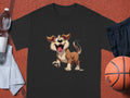 Garment Graphics presents a black T-shirt for dog lovers, featuring a cartoon dog with floppy ears and a happy expression. Styled on an orange surface, its paired with essentials—a water bottle, white towel, black shorts, and an orange basketball.