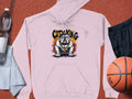 The Garment Graphics pink hoodie featuring a bulldog design with CITY KING text is displayed on a textured surface. Urban edge style is highlighted alongside a clear water bottle, gray towel, black shorts, and an orange basketball.