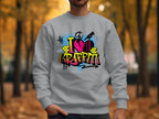 In a park filled with fallen leaves and trees, a person wears a Garment Graphics sweatshirt featuring vibrant graffiti-style art with I Love Graffiti text and a cracked red heart design.
