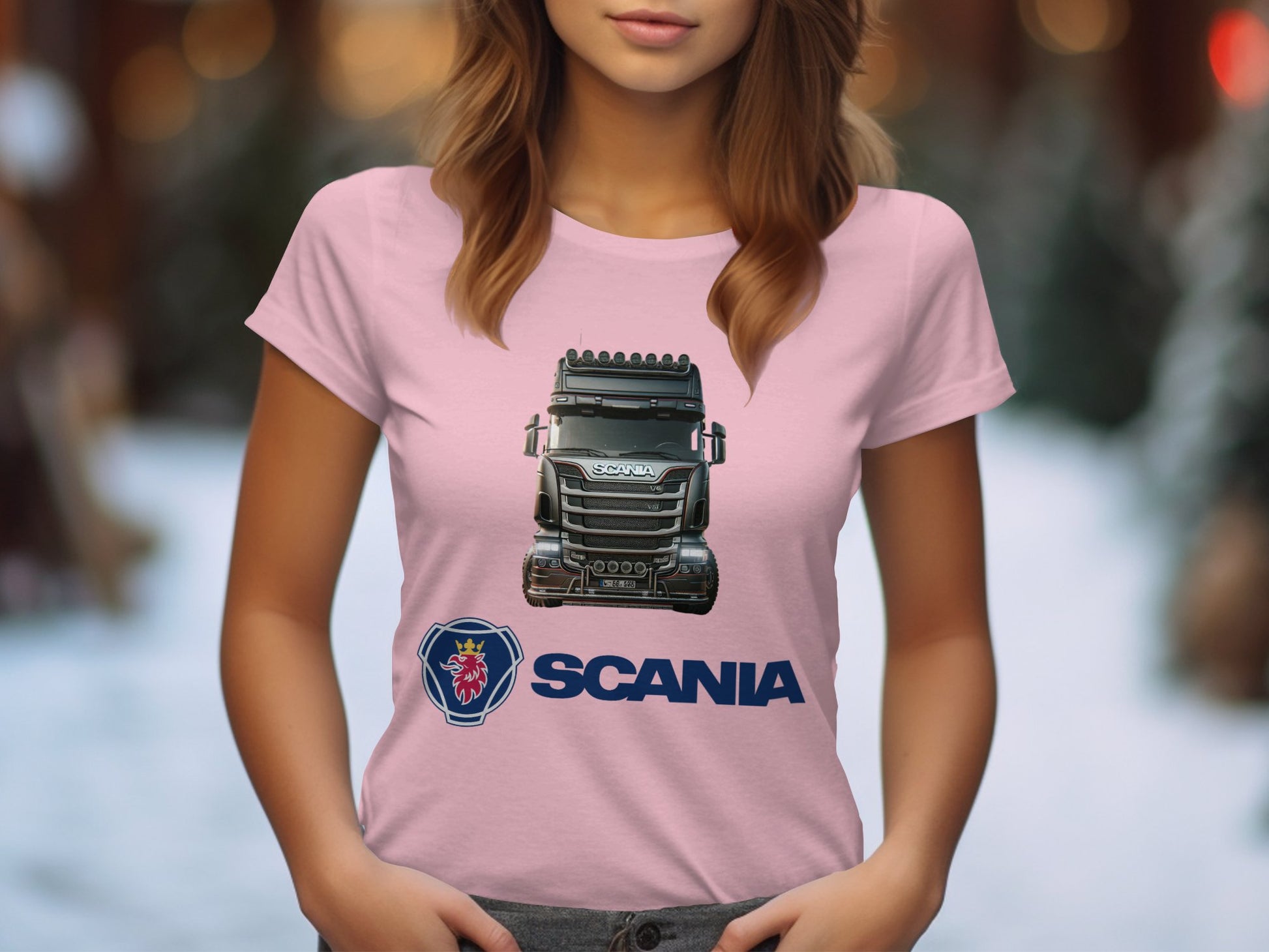 A woman wears a pink Garment Graphics T-shirt, ideal for automotive fans, featuring an illustration of a Scania truck and logo. The blurred backdrop suggests an outdoor scene with trees.