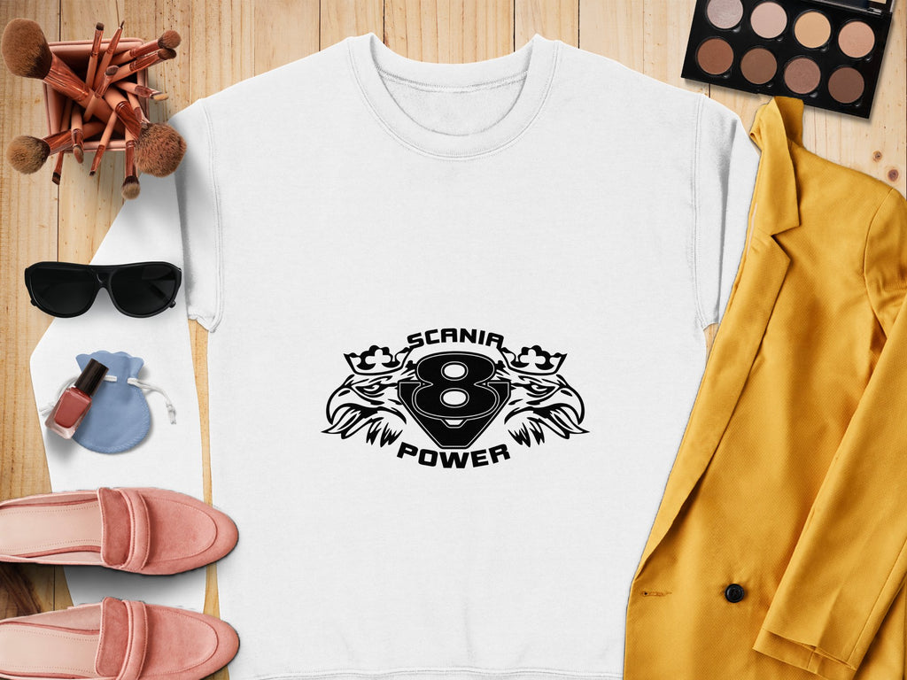 A stylish white Garment Graphics sweatshirt with a cool print of two lions and Scania Power V8 lies on a wooden surface, surrounded by a yellow blazer, pink loafers, sunglasses, makeup brushes, an eyeshadow palette, and perfume.
