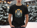A man dressed in a Garment Graphics black T-shirt featuring an owl graphic stands amidst a snowy landscape, exuding artistic flair in the serene setting.