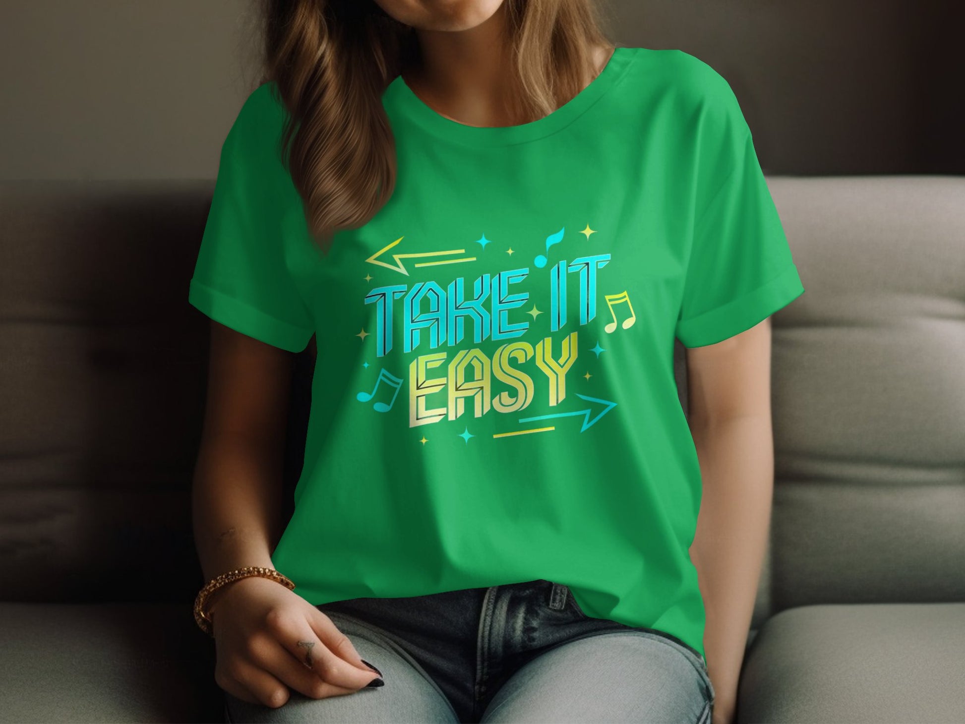 A person with long hair sits on a couch, wearing a vibrant Garment Graphics green t-shirt displaying musical notes, arrows, and Take It Easy in colorful letters. One hand rests on their knee.