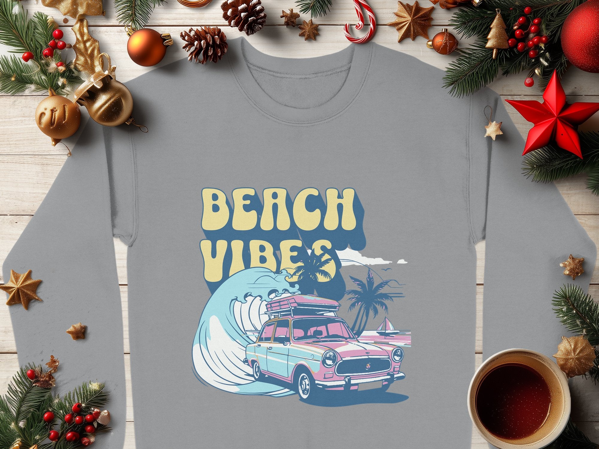 A gray unisex T-shirt by Garment Graphics displays BEACH VIBES above a colorful vintage car illustration on a beach with palm trees and waves, enhanced by festive decorations on wood for a retro roadtrip feel.