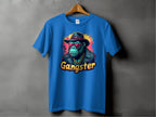 A blue classic-fit T-shirt by Garment Graphics hangs on a wooden hanger against a gray background. It features a gorilla in a black fedora, sunglasses, and gold chain, embodying urban style. The word Gangster completes this bold Gangster Gorilla T-Shirt design.